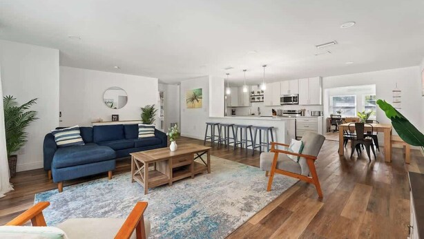A spacious living area with a blue sofa, wooden coffee table, and a dining area with a wooden table and chairs. - Pickleball + Heated Pool | Near Anna Maria (Sarasota)