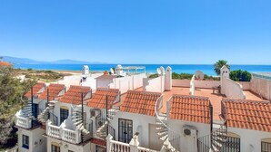 A coastal residential area with terracotta-tiled rooftops, white buildings, and a clear view of the sea.