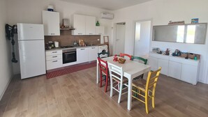 Kompakti keittiö, jossa on valkoiset kaapit, värikkäillä tuoleilla varustettu ruokapöytä, kattotuuletin ja pieni ikkuna.