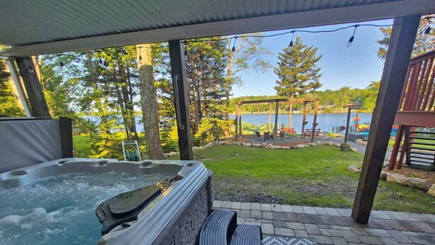 Un jacuzzi con vista a un lago y una terraza con mobiliario exterior.