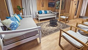 Una habitación acogedora con una cama, un sofá, una mesita y una silla. Hay un televisor montado en la pared y una ventana con cortinas.