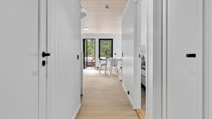 En modern inredning med vita väggar, trägolv och ett centralt, öppet utrymme som leder vidare till en matplats med utsikt över grönområden utanför.