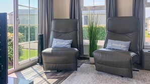 Dos sillones de cuero reclinables con cojines a juego, ubicados en una habitación con ventanas amplias y vista a un jardín.