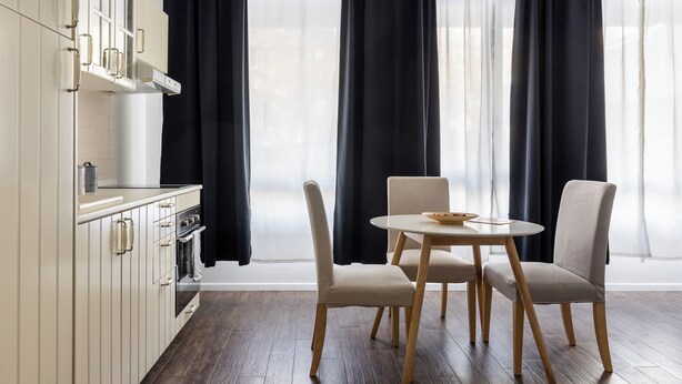 Ett modernt kök med vita skåp, en inbyggd ugn och en matplats med två stolar och ett runt bord.