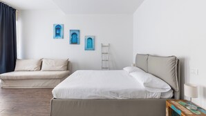 Ett sovrum med en säng, en soffa och ett sängbord med en lampa. Det finns tre blå konstverk på väggen och en stege som lutar mot väggen.