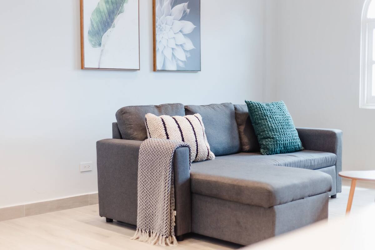 A modern living room with a grey sectional sofa, two framed floral artworks, and a small round table.