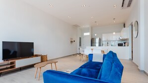 A modern living room with a large flat-screen TV, a blue sofa, and a dining area in the background. - Casa Love by Wynwood House (Panama City)