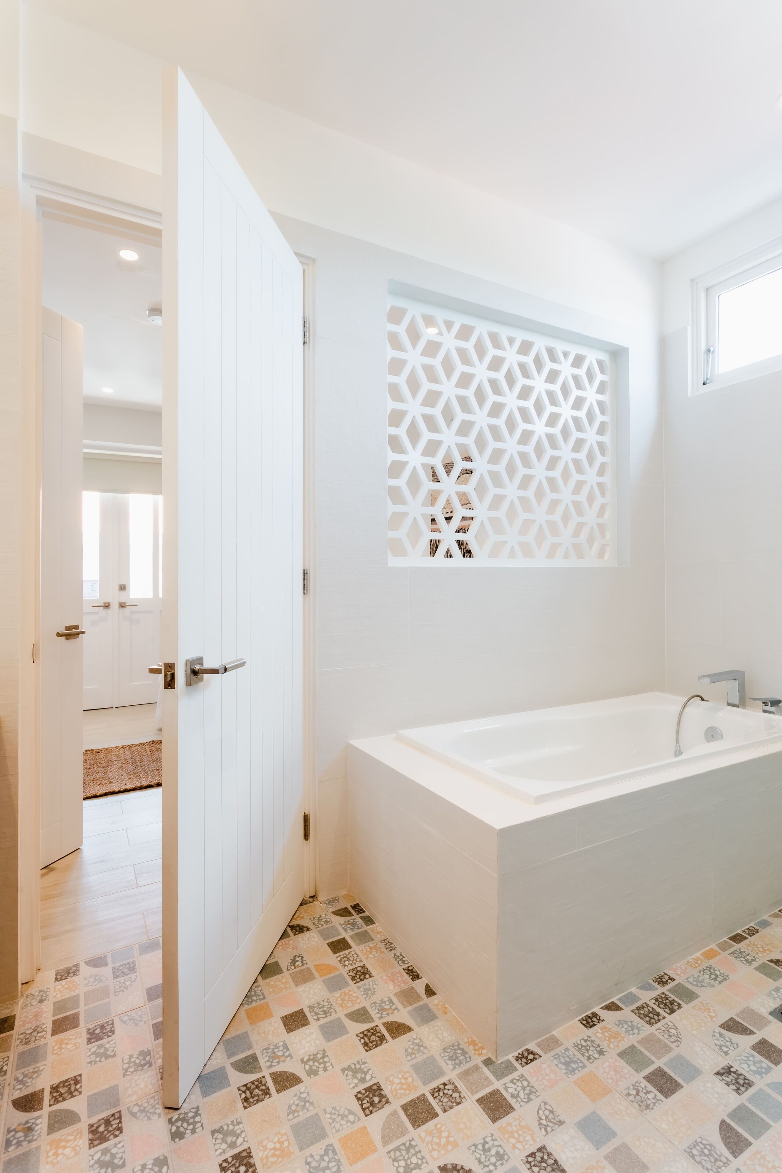Une salle de bain moderne avec une baignoire sur pieds, un panneau mural décoratif aux motifs géométriques et un carrelage au sol.