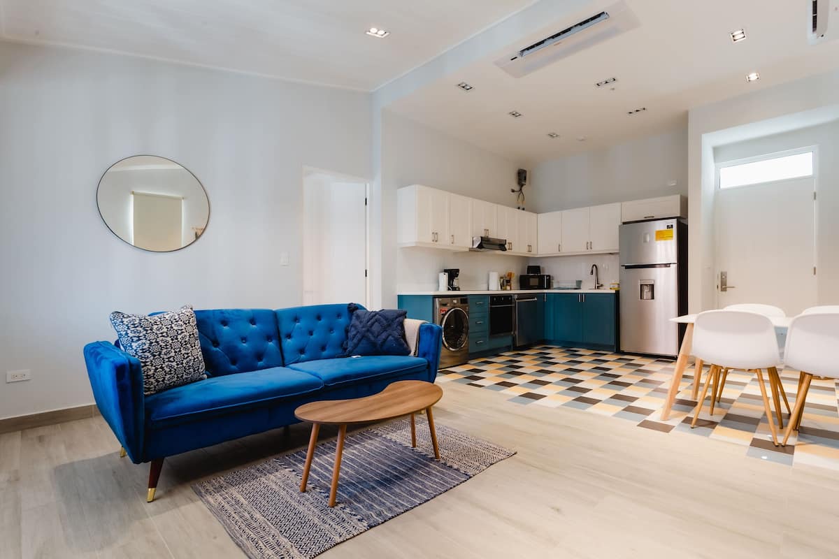 A modern living room with a blue sofa, a round mirror, and a coffee table.