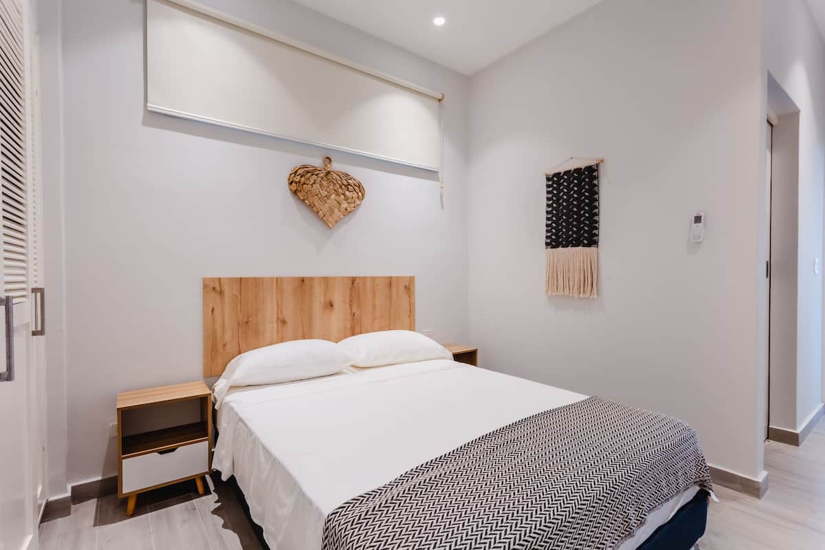 A modern bedroom with a wooden headboard, a white bedspread, and a patterned throw blanket.