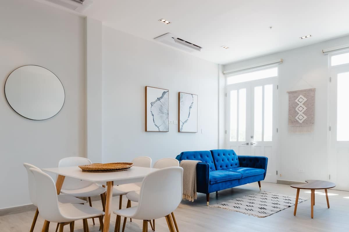 A modern living room with a blue sofa, white chairs, and a dining table.