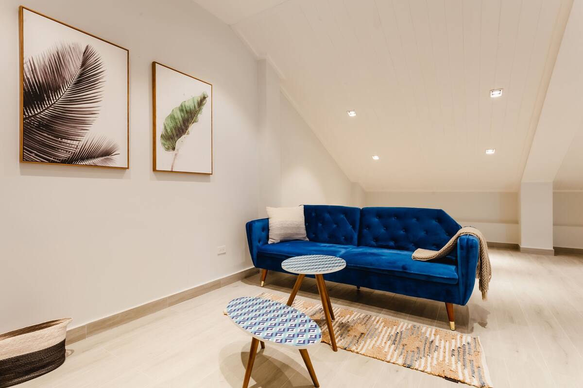 A modern living room with a blue sofa, a round table, and two framed leaf artworks on the wall.