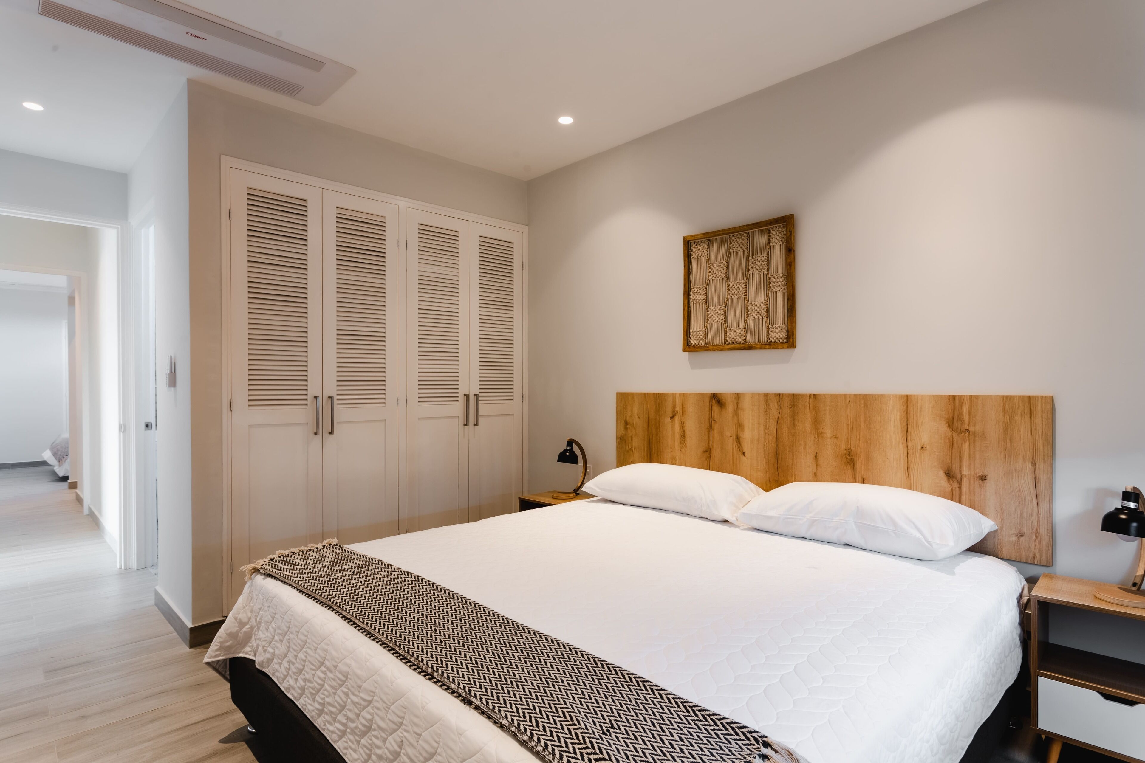 Une chambre à coucher avec un grand lit, une tête de lit en bois, des murs blancs et une porte en bois.