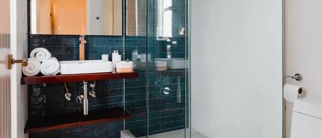 A modern bathroom with a glass-enclosed shower, a white toilet, and a dark tiled backsplash.