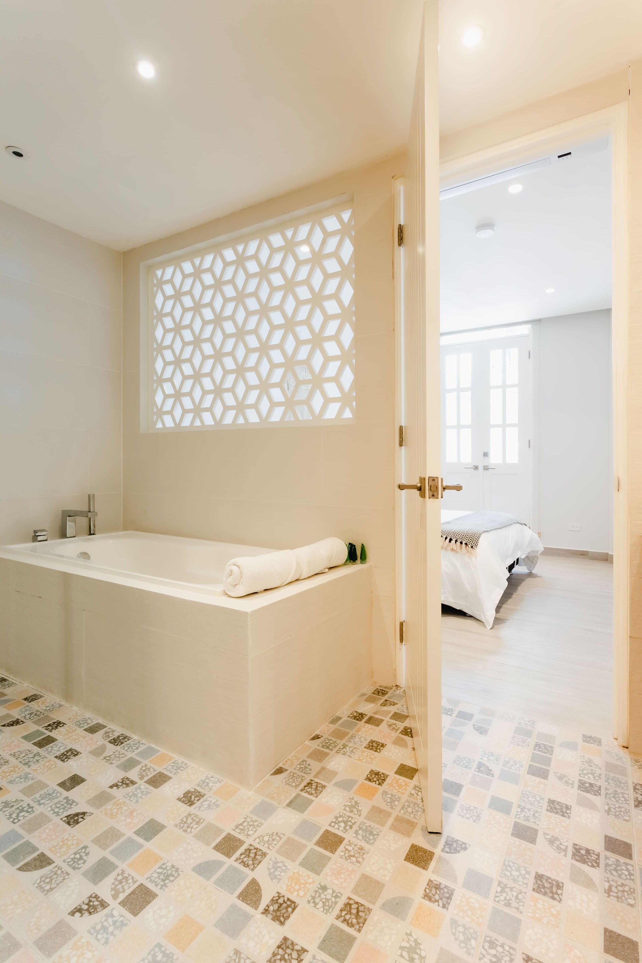 A modern bathroom with a freestanding bathtub, a decorative lattice partition, and a patterned floor.
