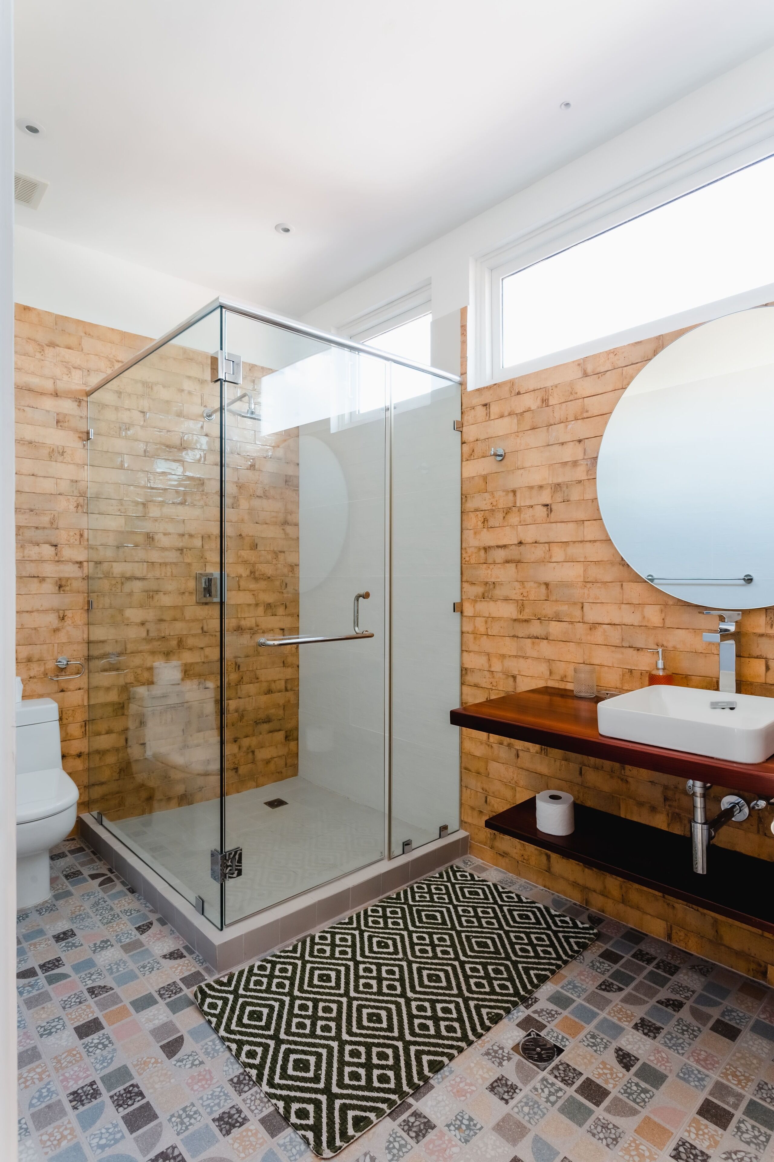 Ein modernes Badezimmer mit einer gläsernen Duschkabine, einem Holzbadezimmer-Möbel und einem Musterfußboden.