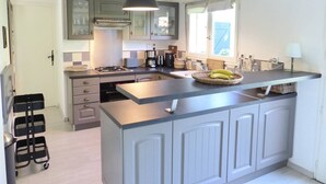 Een moderne keuken met grijze kastjes, een centraal eiland, een gasfornuis en een hangende lamp.