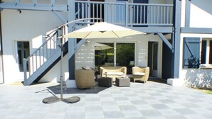 Een overdekt terras met een tafel en stoelen, een pergola en een trap naar een hoger gelegen gedeelte.
