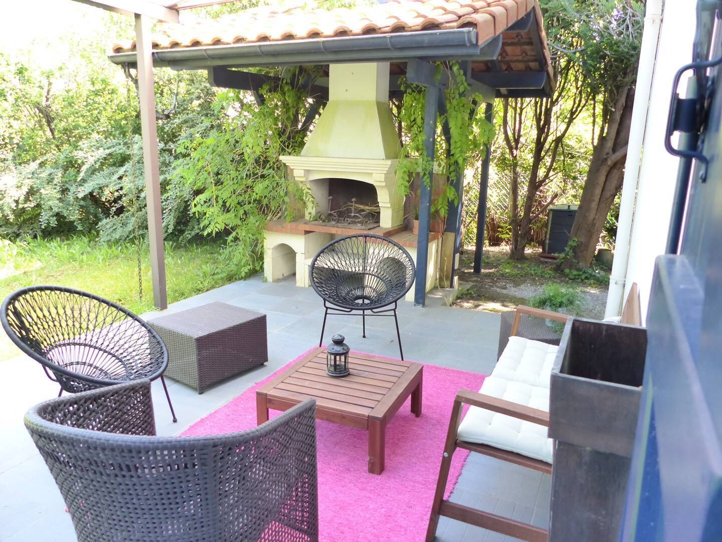 Un patio al aire libre con mobiliario de mimbre, una mesa de madera y una zona de barbacoa.