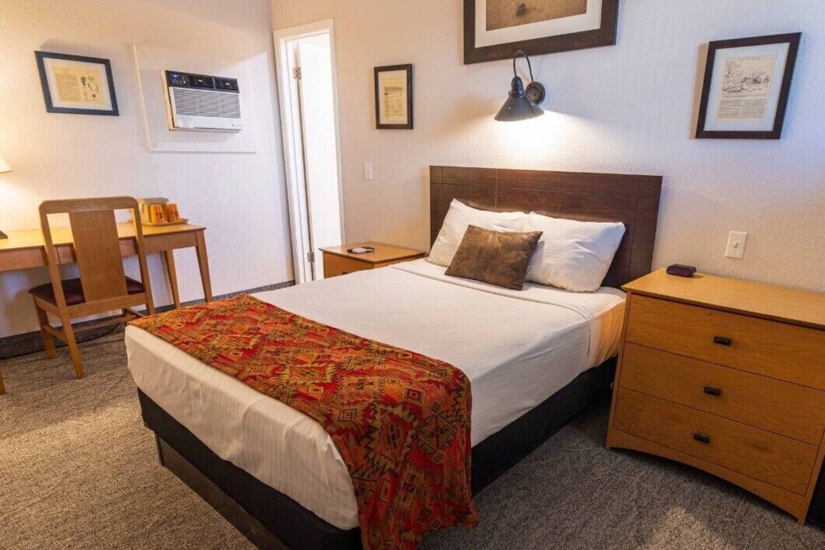 A bedroom with a bed, a desk, a chair, a nightstand, and a dresser.