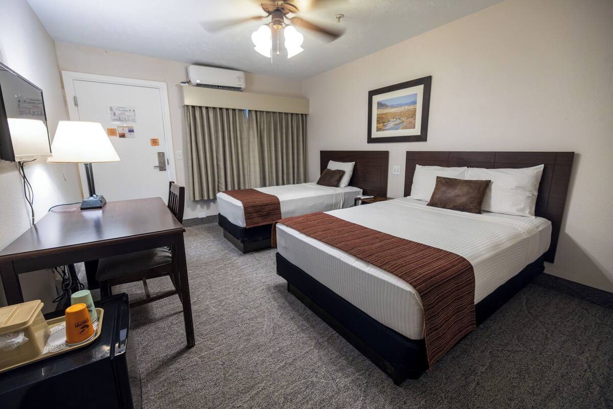 A hotel room with two beds, a desk, a chair, a ceiling fan, and a framed picture on the wall.