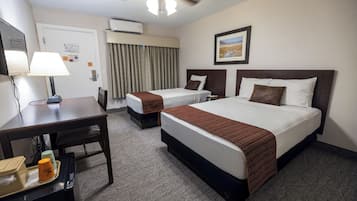 Una habitación de hotel con dos camas, un escritorio, una silla, un ventilador de techo y un cuadro en la pared.
