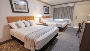 Habitación de hotel con dos camas, un escritorio, una silla, una lámpara y una ventana con cortinas.