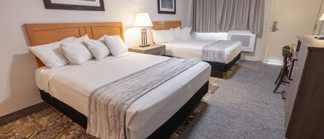 A hotel room with two beds, a desk, a chair, a lamp, and a window with curtains.