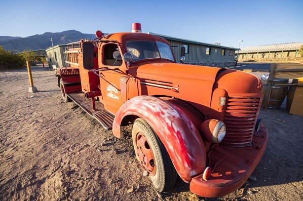 An old orange truck parked on a dirt surface with mountains in the background. - Stovepipe Wells Village Hotel - Inside The Park (Death Valley)