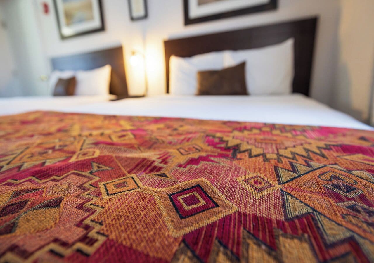 A bed with a patterned bedspread, a headboard, and two bedside lamps.