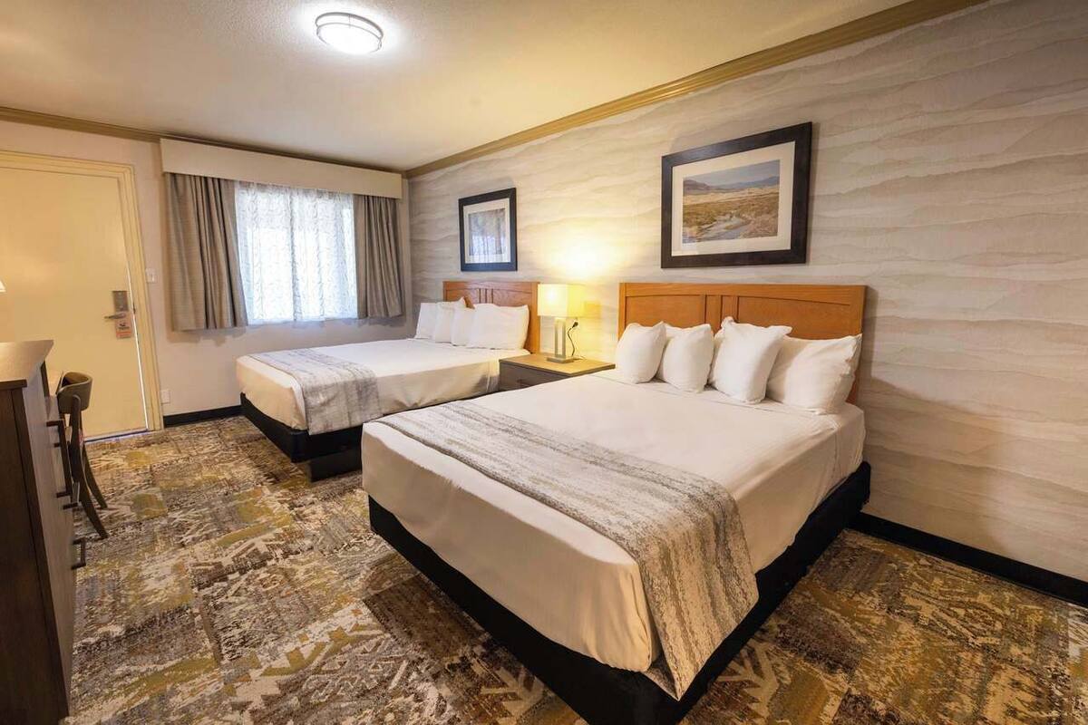 A hotel room with two beds, a desk, and a chair.
