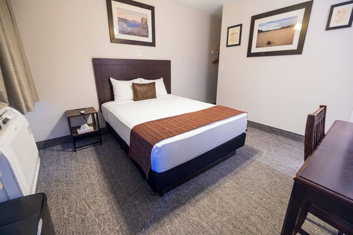 A hotel room with a bed, a nightstand, a desk, and a chair.