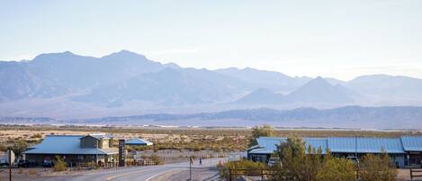 A road curving through a desert landscape with mountains in the background. There are buildings with blue roofs along the roadside.