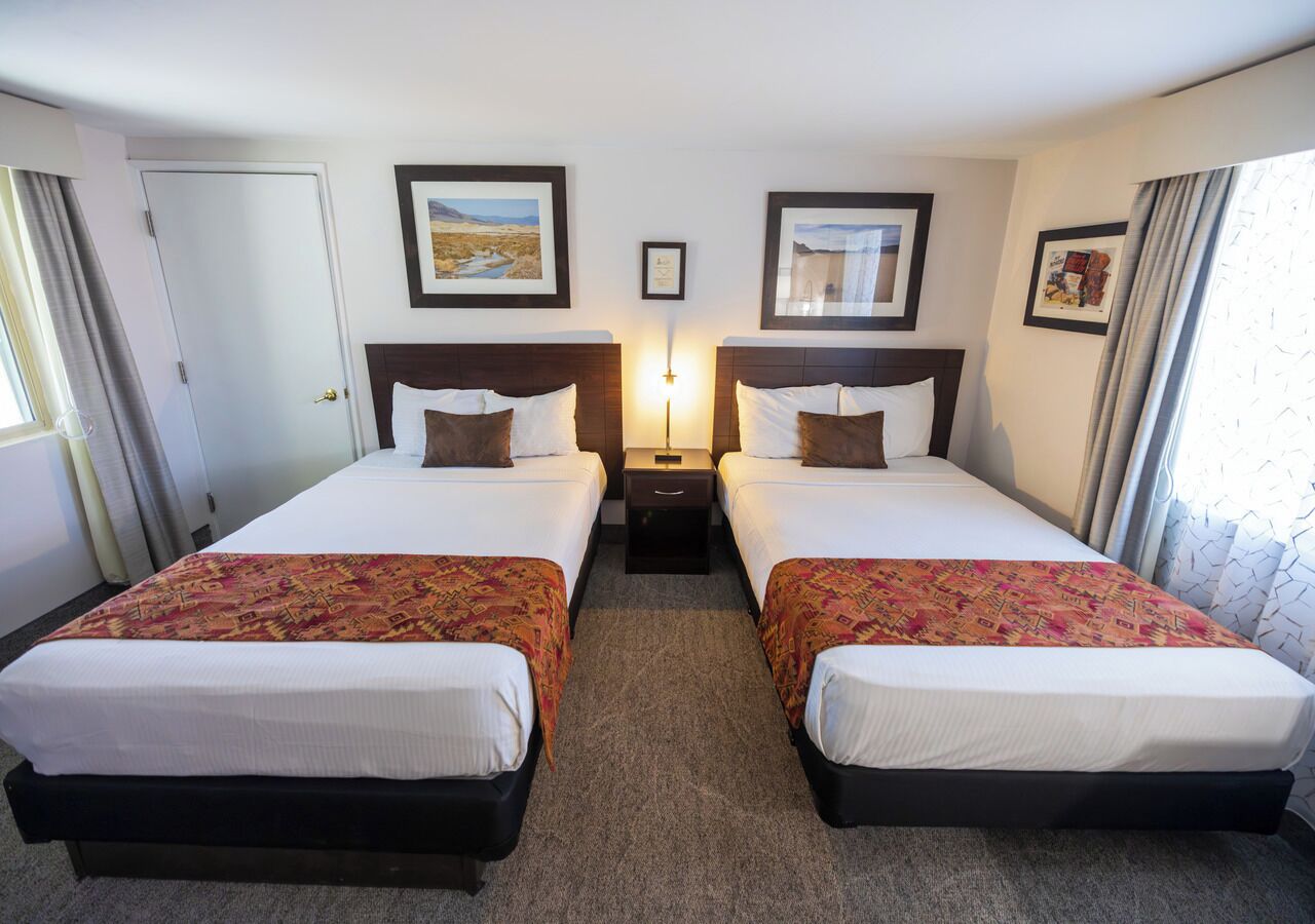 A hotel room with two beds, a nightstand, and framed pictures on the walls.