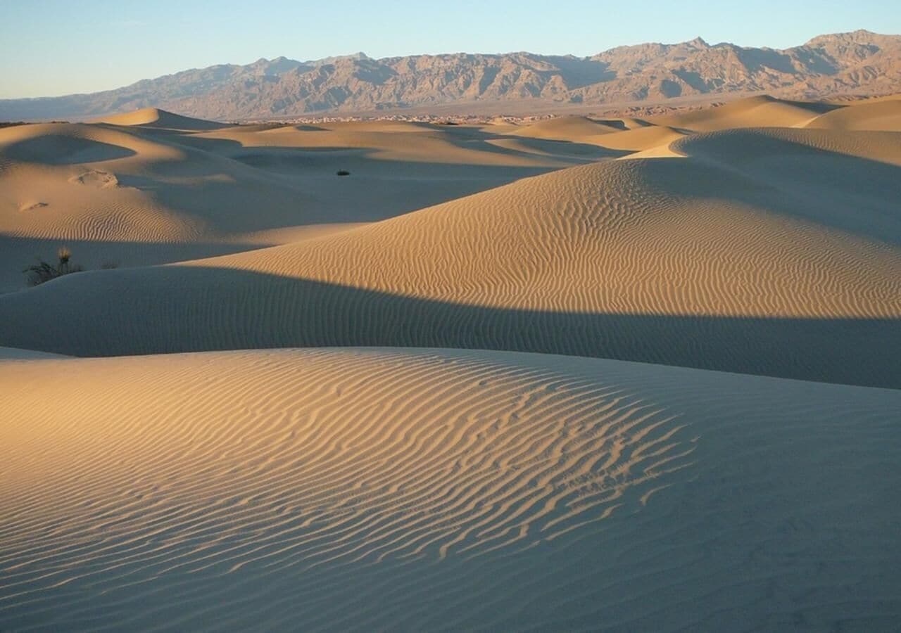 Paisaje desértico con dunas de arena y montañas al fondo.