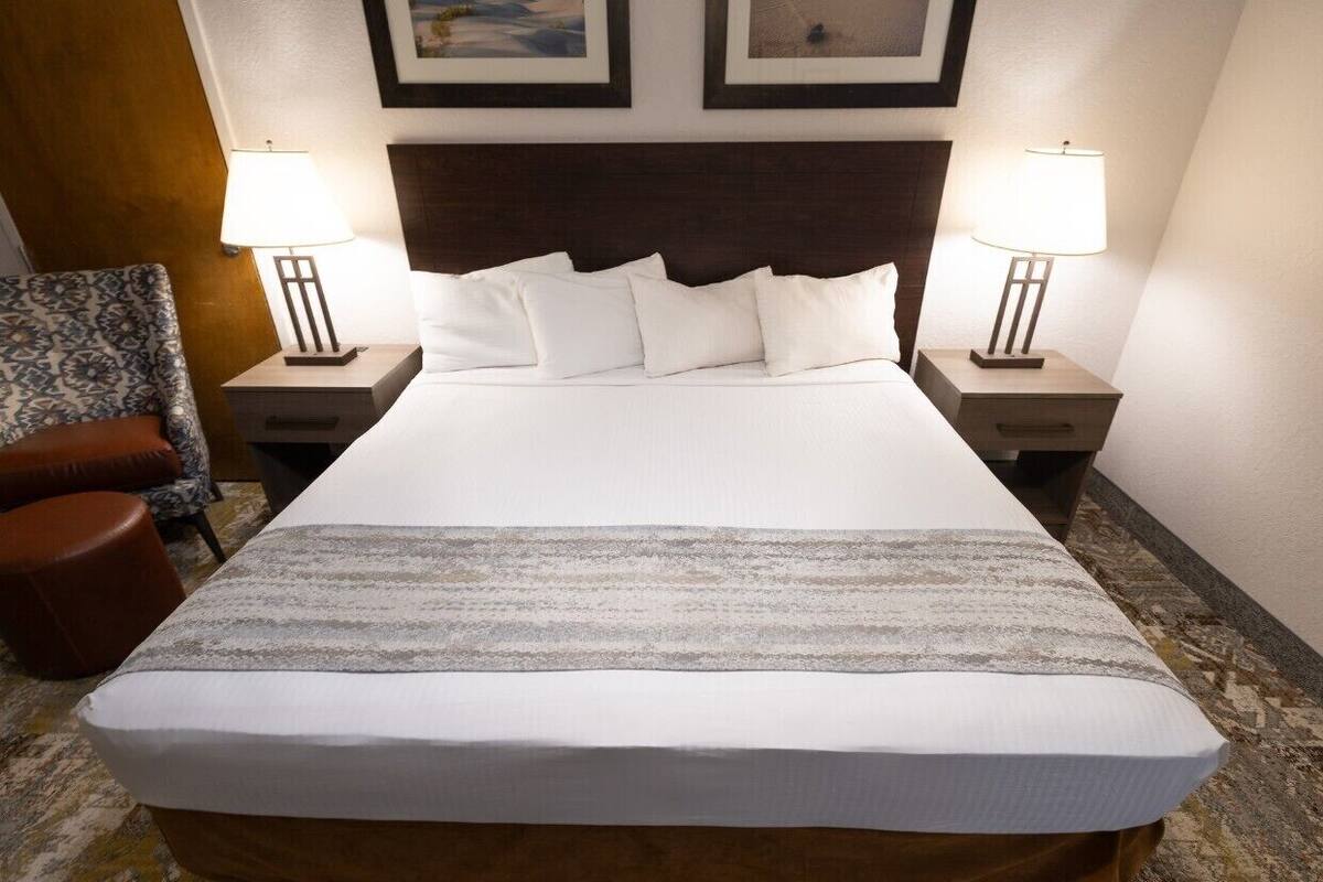 A hotel room with a large bed, two bedside tables with lamps, a patterned rug, and a brown leather chair.