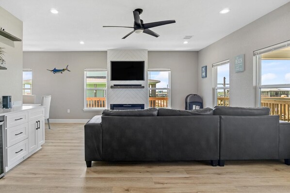 Een moderne woonkamer met een hoekbank, een flatscreen-tv, een plafondventilator en grote ramen met uitzicht op het strand.