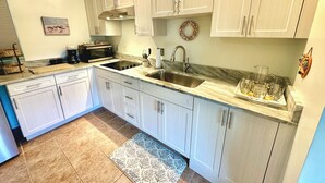 A modern kitchen with white cabinets, a stainless steel sink, a microwave, and a gas stove. - Susannah Riverside Apartment - Tranquil getaway for 2 (Fort Pierce)