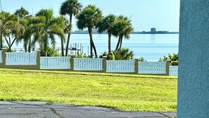A view of a waterfront property with a grassy lawn, palm trees, and a white fence. - Susannah Riverside Apartment - Tranquil getaway for 2 (Fort Pierce)