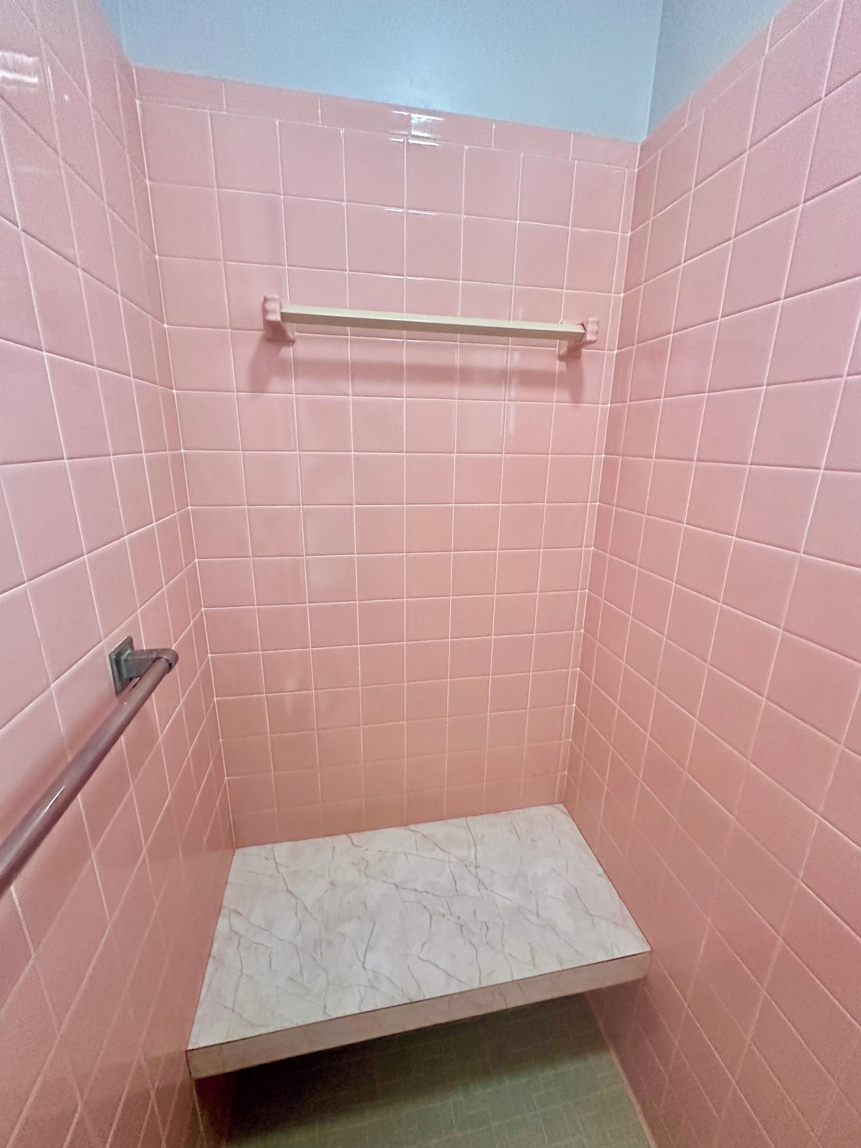 A small, tiled shower area with a metal grab bar and a shelf.