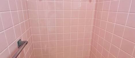 A small, tiled shower area with a metal grab bar and a shelf.