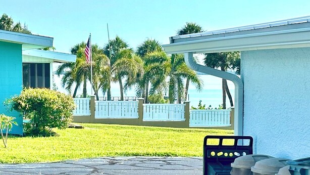 A parking area with a row of trash bins, a white fence, and palm trees in the background. - Susannah Riverside Apartment - Tranquil getaway for 2 (Fort Pierce)