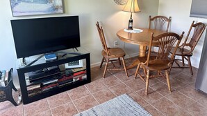 A living room with a flat-screen TV, wooden dining table, and chairs. - Susannah Riverside Apartment - Tranquil getaway for 2 (Fort Pierce)