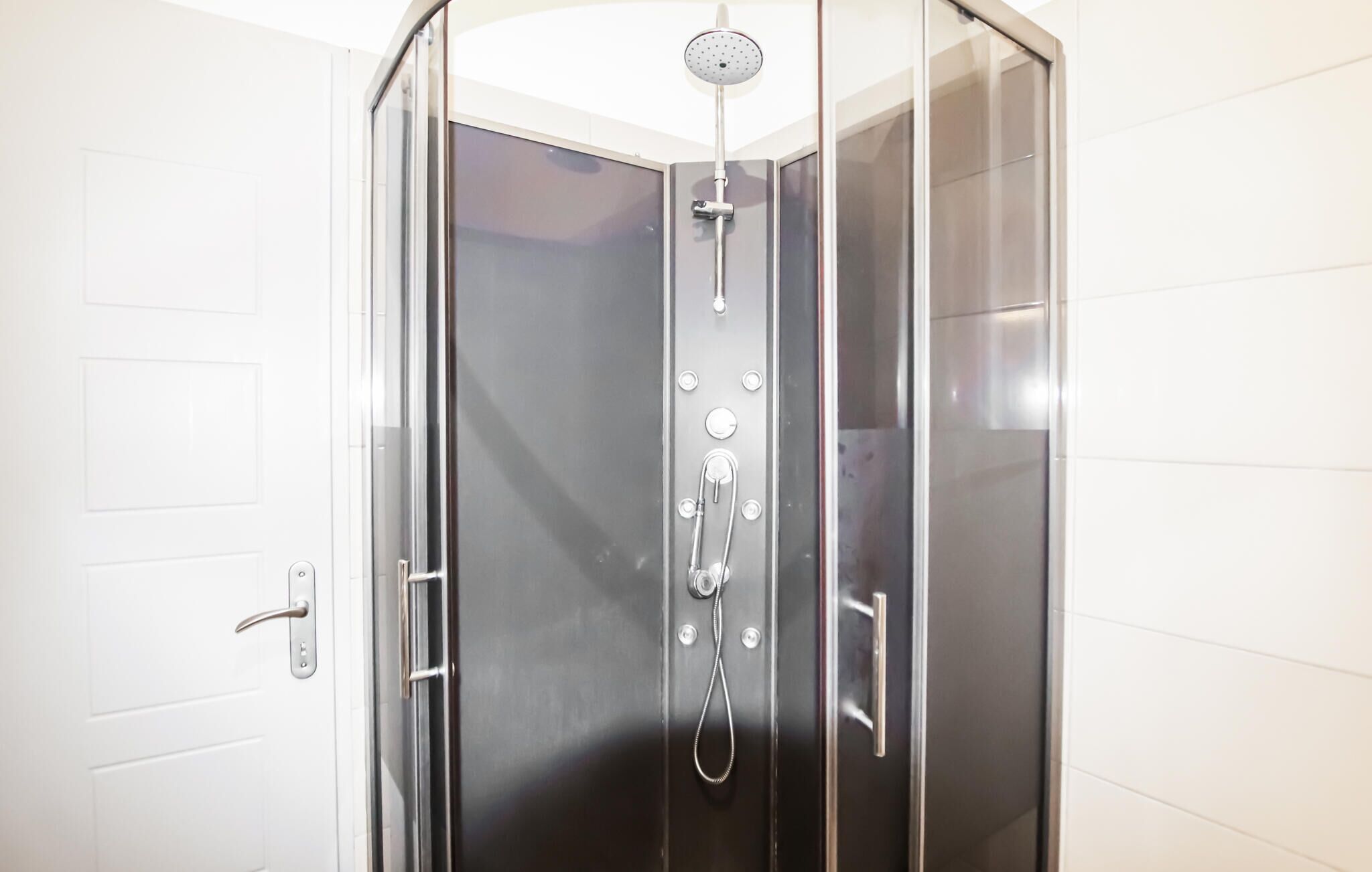 A modern, enclosed shower with a glass door, a handheld showerhead, and a control panel.