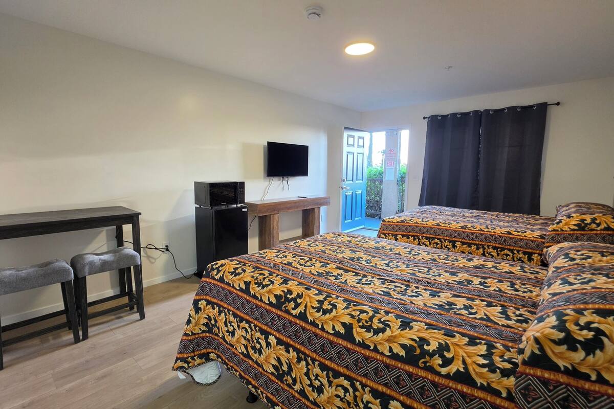 A bedroom with a bed, a desk, a TV, and a door leading outside.