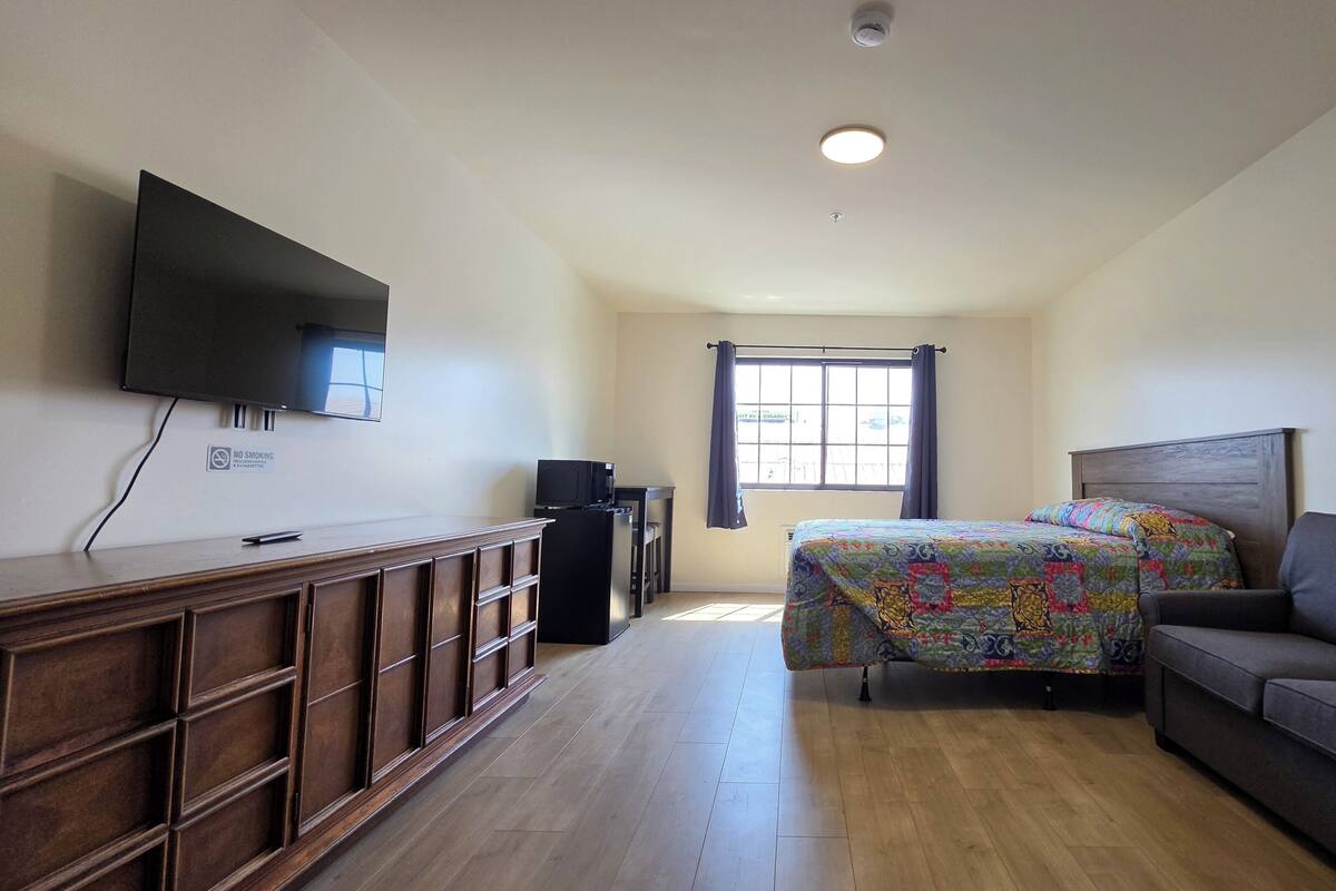 A room with a bed, a sofa, a TV mounted on the wall, and a window with curtains.