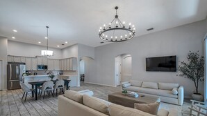 A spacious living area with a large sofa, a dining table with chairs, a kitchen area with cabinets, and a chandelier. - Large 5 bedroom 3 full bath house close to beaches, shopping  and parks. (Parrish)