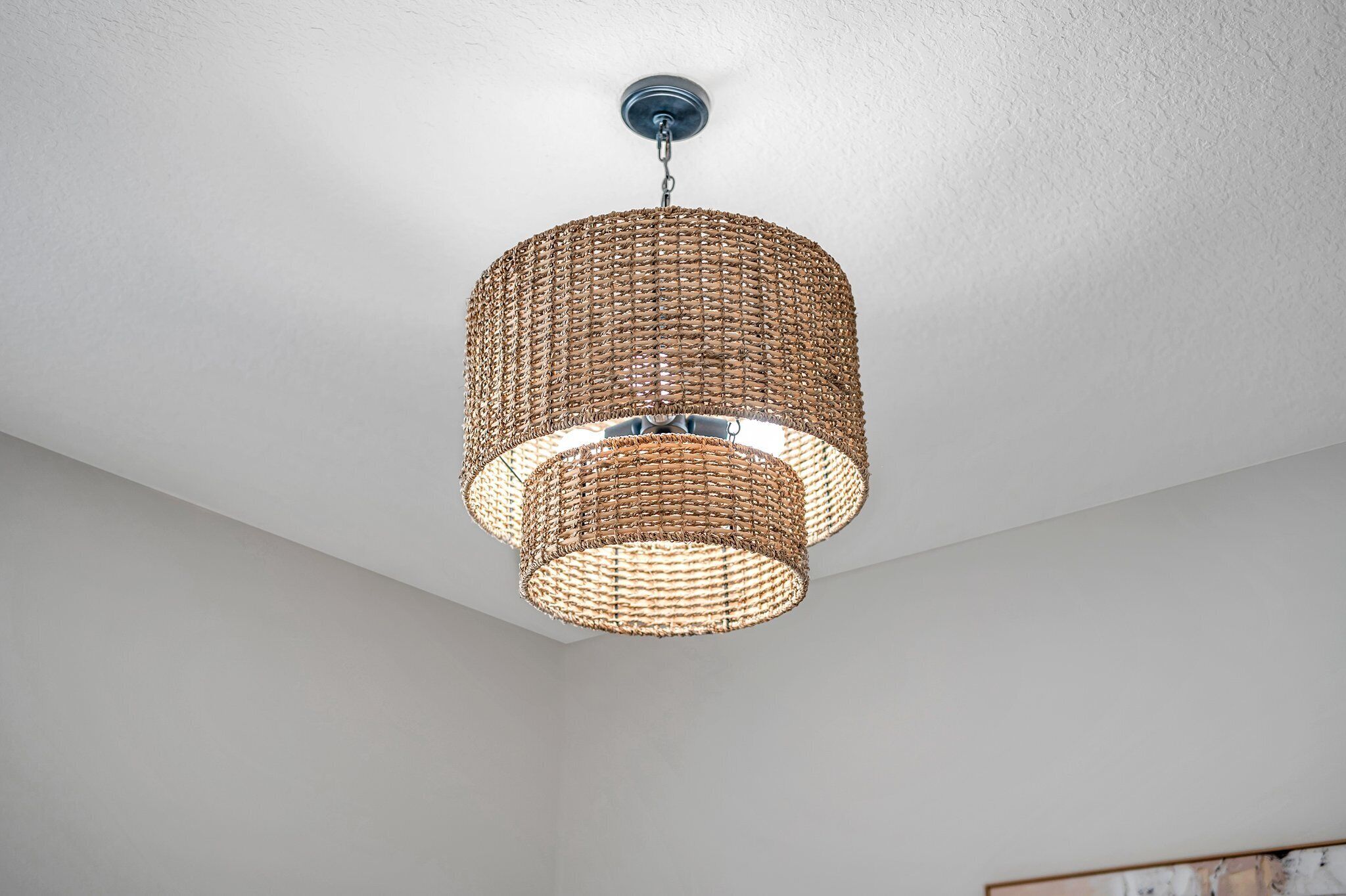 En vævet pendel lampe i et rum med hvide vægge og synligt loft.