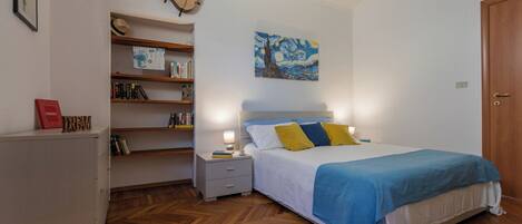Une chambre à coucher avec un lit, une table de chevet, une bibliothèque, une guitare et un tableau accroché au mur.
