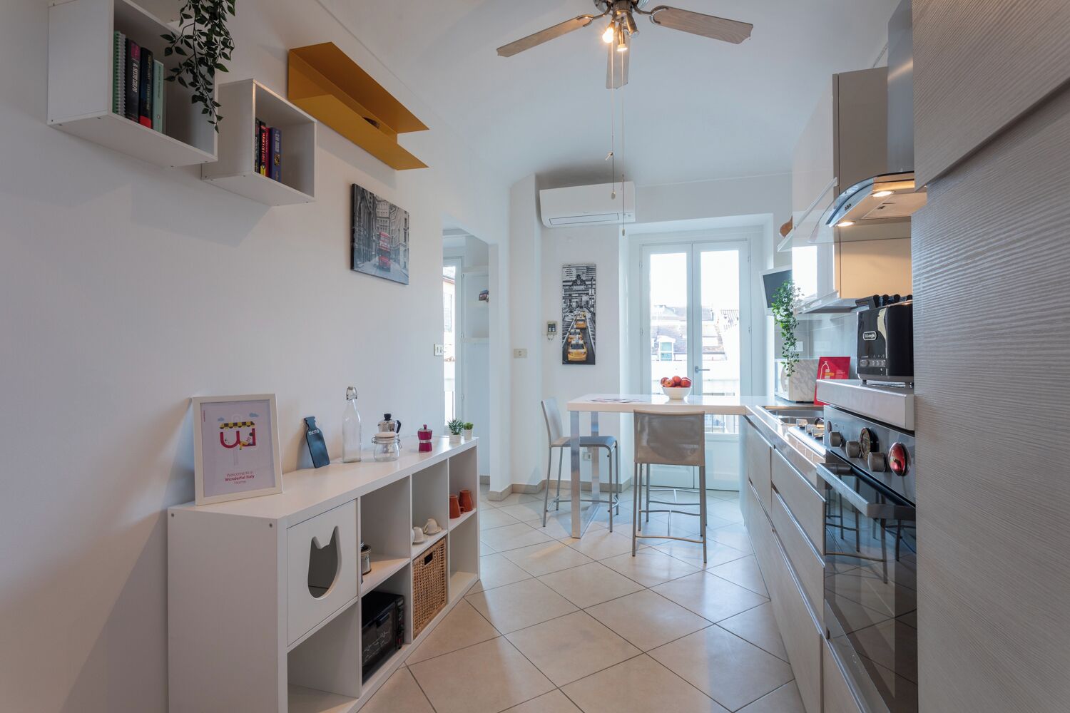 Une cuisine moderne avec des meubles blancs, un coin repas doté d’une table et de chaises blanches, et un ventilateur de plafond.